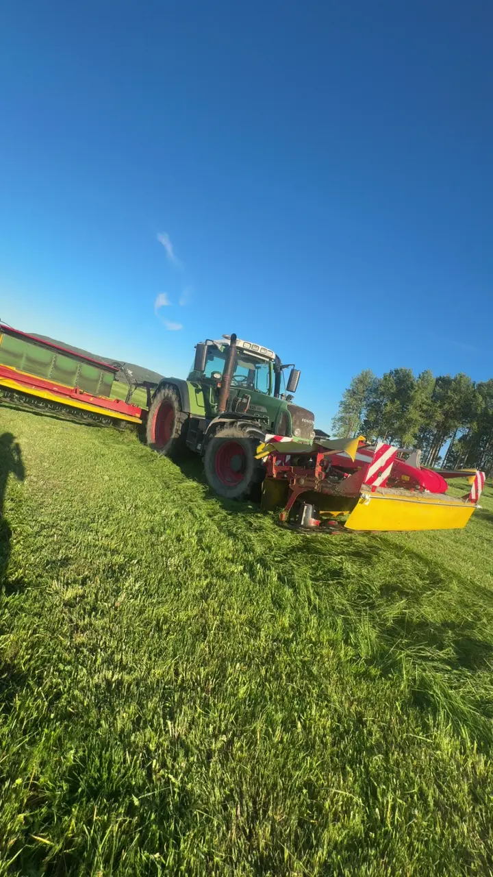 Traktor med slåtterredskap arbetar på ett grönt fält.